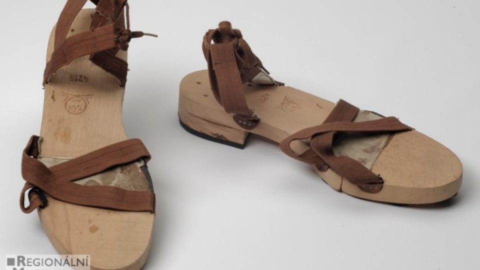 Dámské sandály s dřevěnou podešví dělenou a spojenou kůží a s hnědými plátěnými pásky na zavazování na tkaničku namísto přezky. Vyráběné jako nouzová obuv za druhé světové války (např. i firma Baťa)