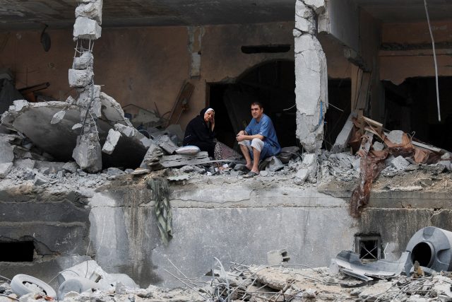 Palestinci sedí mezi troskami poškozené budovy po izraelských úderech ve městě Gaza | foto: Mohammed Salem,  Reuters